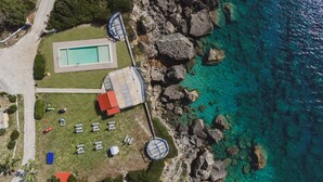 Ett flygbildsbild av en fastighet vid kusten med en swimmingpool, en tennisbana och en lusthus.