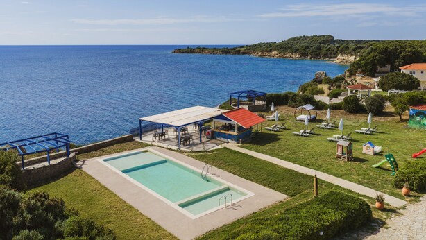 Una piscina con vista al mar, un área de estar cubierta y un pequeño edificio con techo rojo.