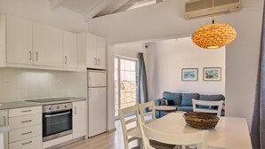 Una cocina moderna con armarios blancos, horno empotrado y comedor con mesa y sillas blancas.