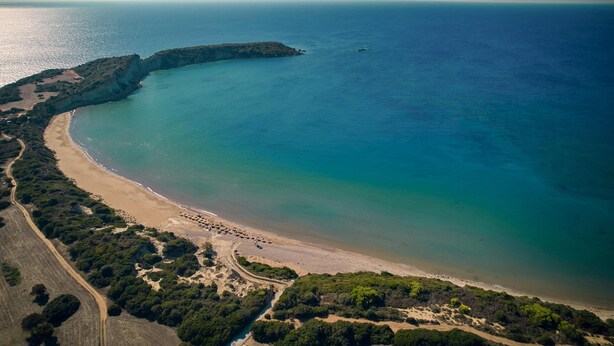 An aerial view of a coastal area with a beach, a small peninsula, and a clear sky.
