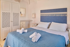 A neatly made bed with a blue quilt, two rolled towels, and a headboard with a fringe detail. - Villa Lito  Periyali (Zakynthos)