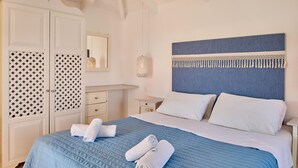 A neatly made bed with blue bedding and white pillows, a bedside table with a lamp, and a wardrobe with patterned doors. - Villa Ourania Periyali (Zakynthos)