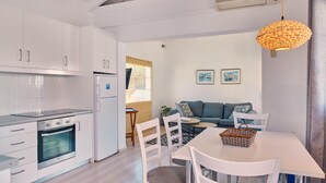 A modern kitchen with white cabinets, a built-in oven, and a dining area with a white table and chairs. - Villa Ourania Periyali (Zakynthos)