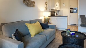 A modern living room with a grey sofa, a round black coffee table, and a kitchen in the background. - Fiedler Oase vacation apartment on Sylt - comfort close to the beach (Sylt)