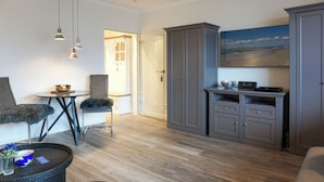 A modern living room with a dining area, grey cabinets, a painting of a beach, and a small table with a bowl. - Fiedler Oase vacation apartment on Sylt - comfort close to the beach (Sylt)