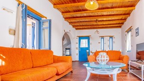 Un salón amplio con sofás color naranja, una mesa de centro de cristal y techo de madera.