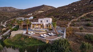 A modern villa with a pool, sun loungers, and a stone pathway. - Luxury Villa Delphinus - AllParos Villas (Paros)