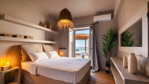 A bedroom with a bed, bedside tables, a hanging light fixture, a potted plant, and a view through an open door. - Luxury Villa Delphinus - AllParos Villas (Paros)