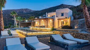 A modern villa with a pool, lounge chairs, and a stone pathway leading to the entrance. - Luxury Villa Delphinus - AllParos Villas (Paros)