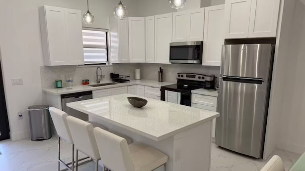 A modern kitchen with white cabinetry, stainless steel appliances, a central island with bar stools, and pendant lighting. - Chic New Build Duplex /King Suite & Cover Lanai (Punta Gorda)