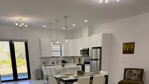 A modern kitchen with white cabinets, a dining area with a table and chairs, and a living area with a sofa. - Chic New Build Duplex /King Suite & Cover Lanai (Punta Gorda)