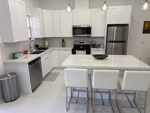 A modern kitchen with white cabinets, stainless steel appliances, and a central island with bar stools. - Chic New Build Duplex /King Suite & Cover Lanai (Punta Gorda)