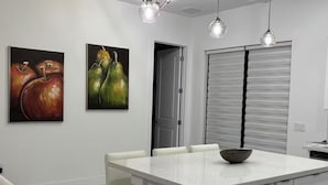 A modern kitchen with white cabinetry, a central island with a bowl, pendant lighting, and two paintings on the wall. - Chic New Build Duplex /King Suite & Cover Lanai (Punta Gorda)