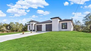 A modern two-story house with a large garage, a well-maintained lawn, and a clear blue sky. - Chic New Build Duplex /King Suite & Cover Lanai (Punta Gorda)
