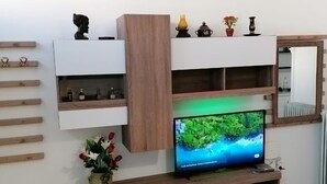 A modern living room with a flat-screen TV, wooden shelves, and decorative items. - Studio Orion - AllParos Villas (Paros)