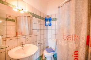 Et badeværelse med håndvask, toilet og bruseforhæng.