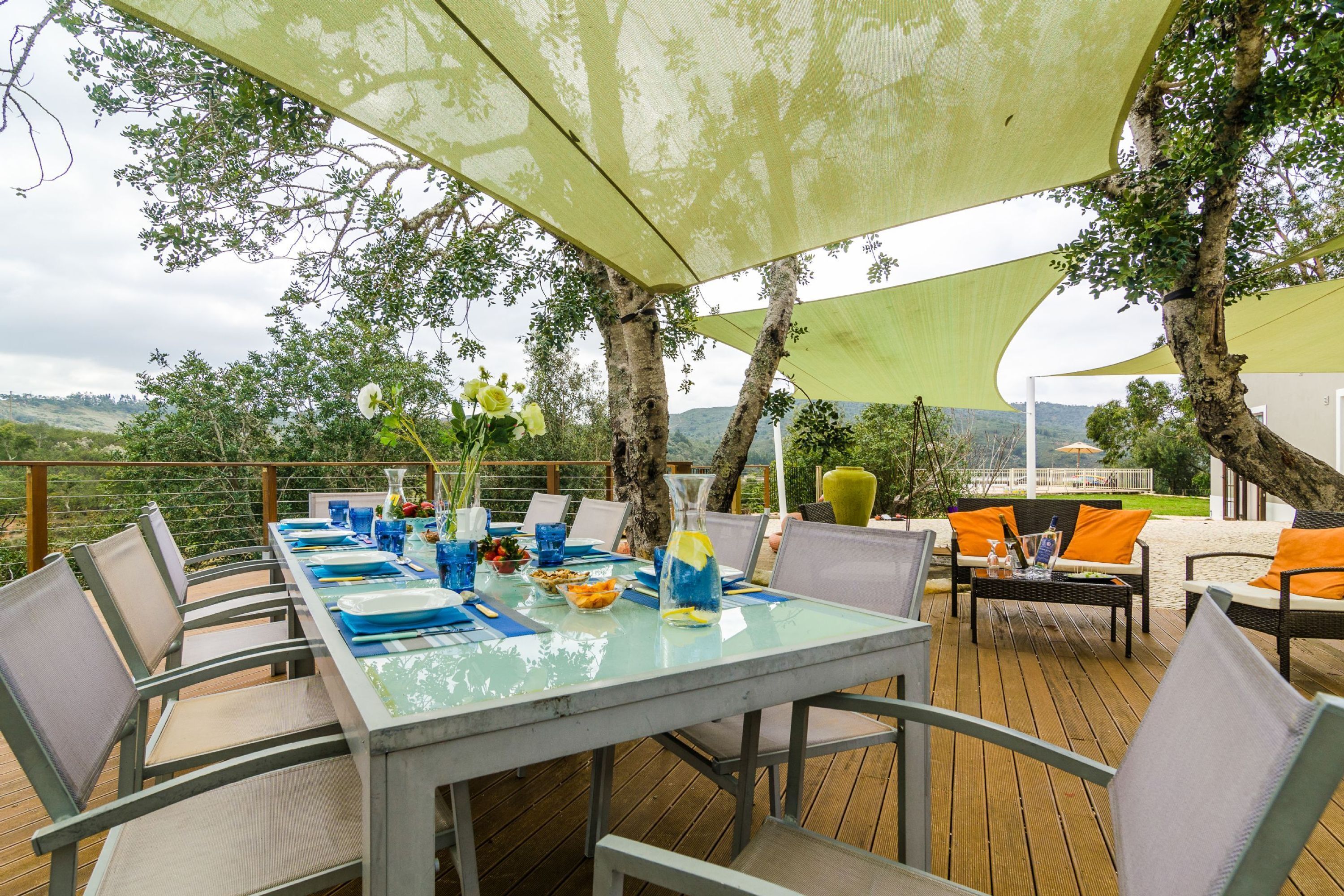 Un'area pranzo all'aperto con un tavolo apparecchiato per quattro persone, circondato da sedie e riparato da un'ampia tenda.