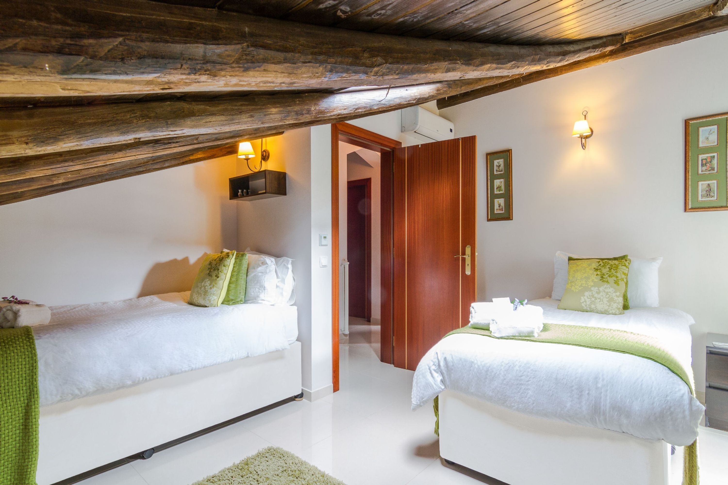 A bedroom with two beds, a wooden ceiling, and a hallway leading to another room.