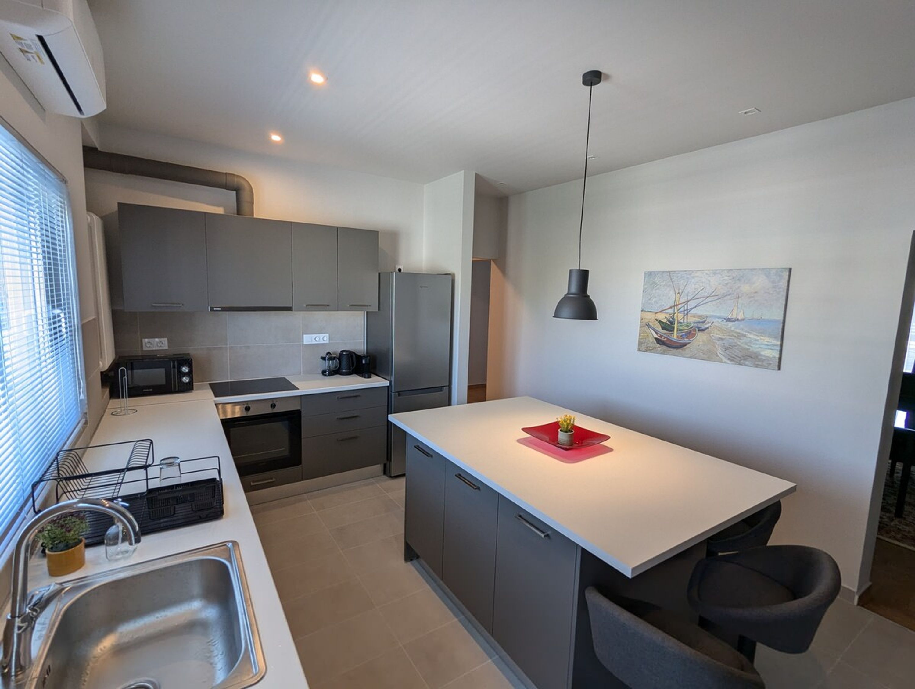 A modern kitchen with grey cabinets, a stainless steel refrigerator, a microwave, and a sink.