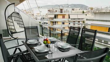 Een balkon met een eettafel voor vier personen, omringd door stoelen, met een hangstoel en uitzicht op de stad.