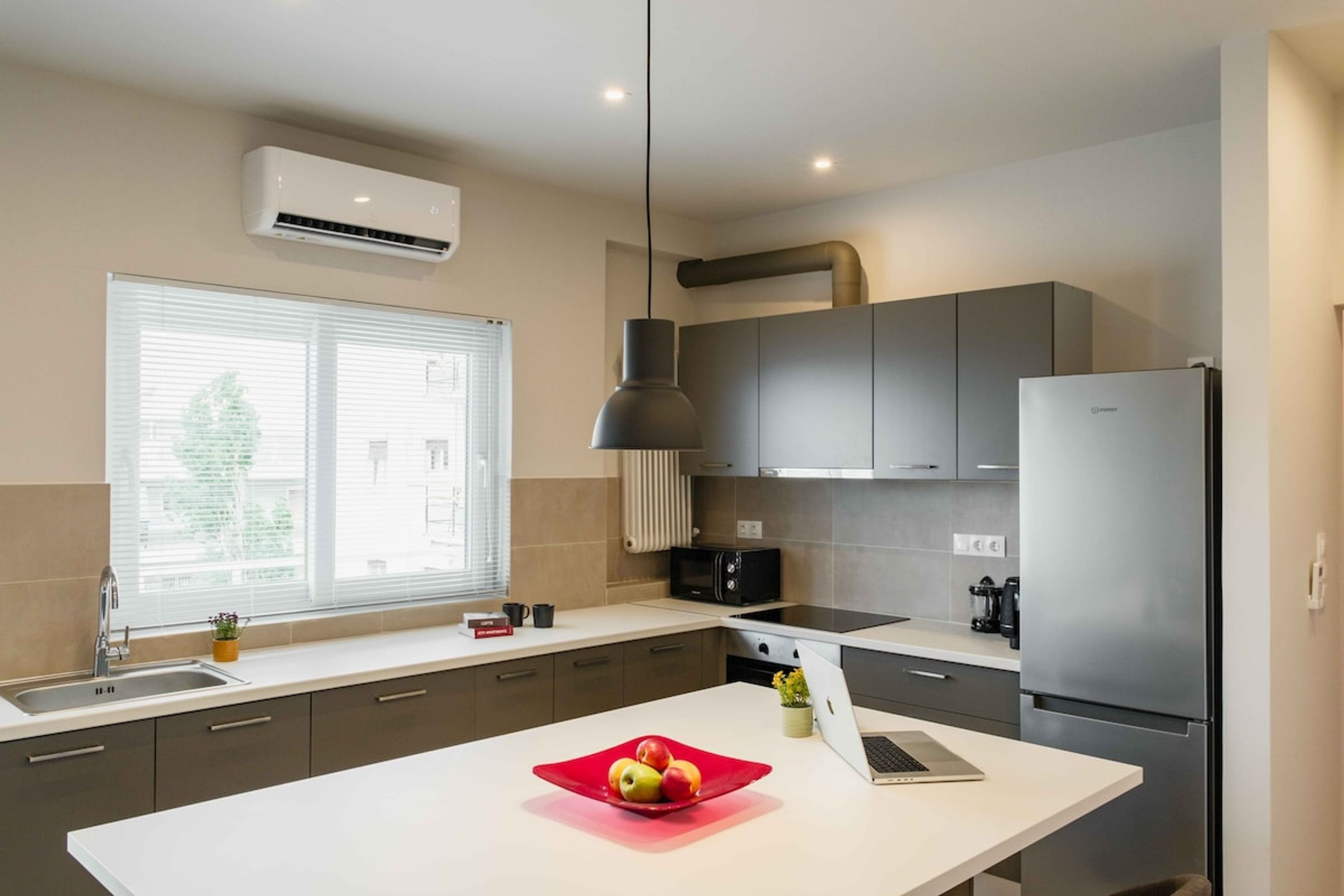 Een moderne keuken met een centraal eiland, een ingebouwde oven, een koelkast en een raam met zonwering.