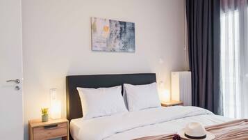 Una habitación de hotel con cama, mesitas de noche, una obra de arte en la pared y una ventana con cortinas.