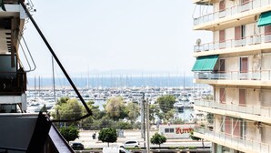 A view from a balcony overlooking a marina with boats, a white van, and a building with a green awning. - Spacious and sunlit seaside flat (Alimos)
