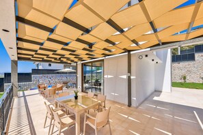 An outdoor patio with a glass wall, wicker furniture, and a view of the city. - Villa Etoo in Yeşilköy Mahallesi (Yeşilköy Mahallesi)