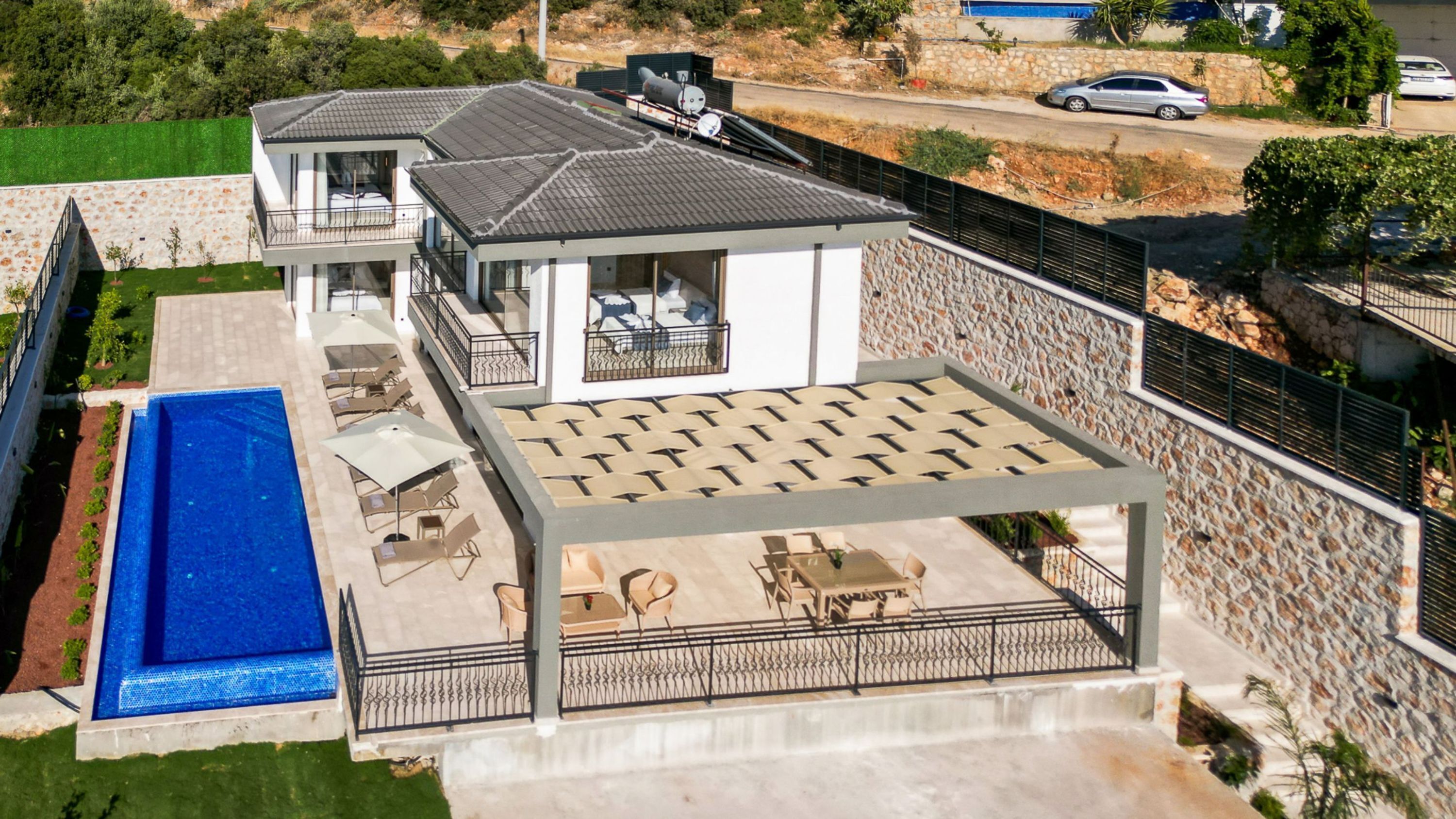 Una casa moderna de dos pisos amb piscina, zona d'estar a l'exterior i mur de pedra.