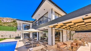 Ein modernes Haus mit Swimmingpool, Sitzgelegenheit im Freien und einer überdachten Terrasse.