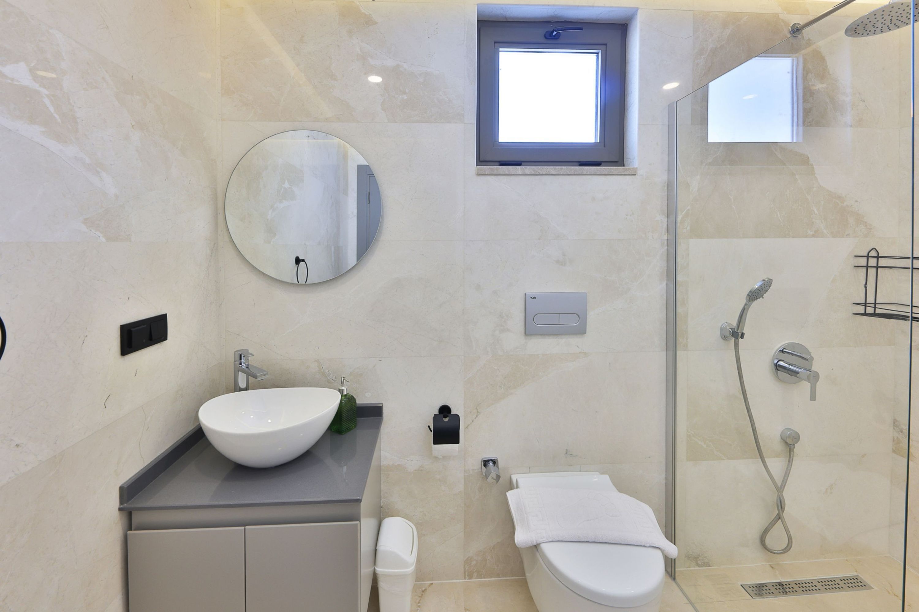 A modern bathroom with a round mirror, a sink, a toilet, and a glass-enclosed shower area.
