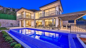 A modern two-story house with a swimming pool, outdoor seating, and a view of the surrounding landscape. - Villa Maranga in Kalkan (Kalkan)