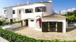 A white two-story house with a tiled roof, a small attached structure with a glass door, and a white picket fence. - Villa Praia in Albufeira (Albufeira)