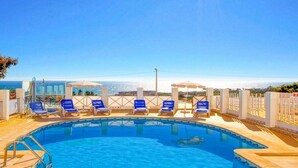 A swimming pool with blue chairs and umbrellas, surrounded by a white fence, overlooking a body of water. - Villa Mar in Albufeira (Albufeira)