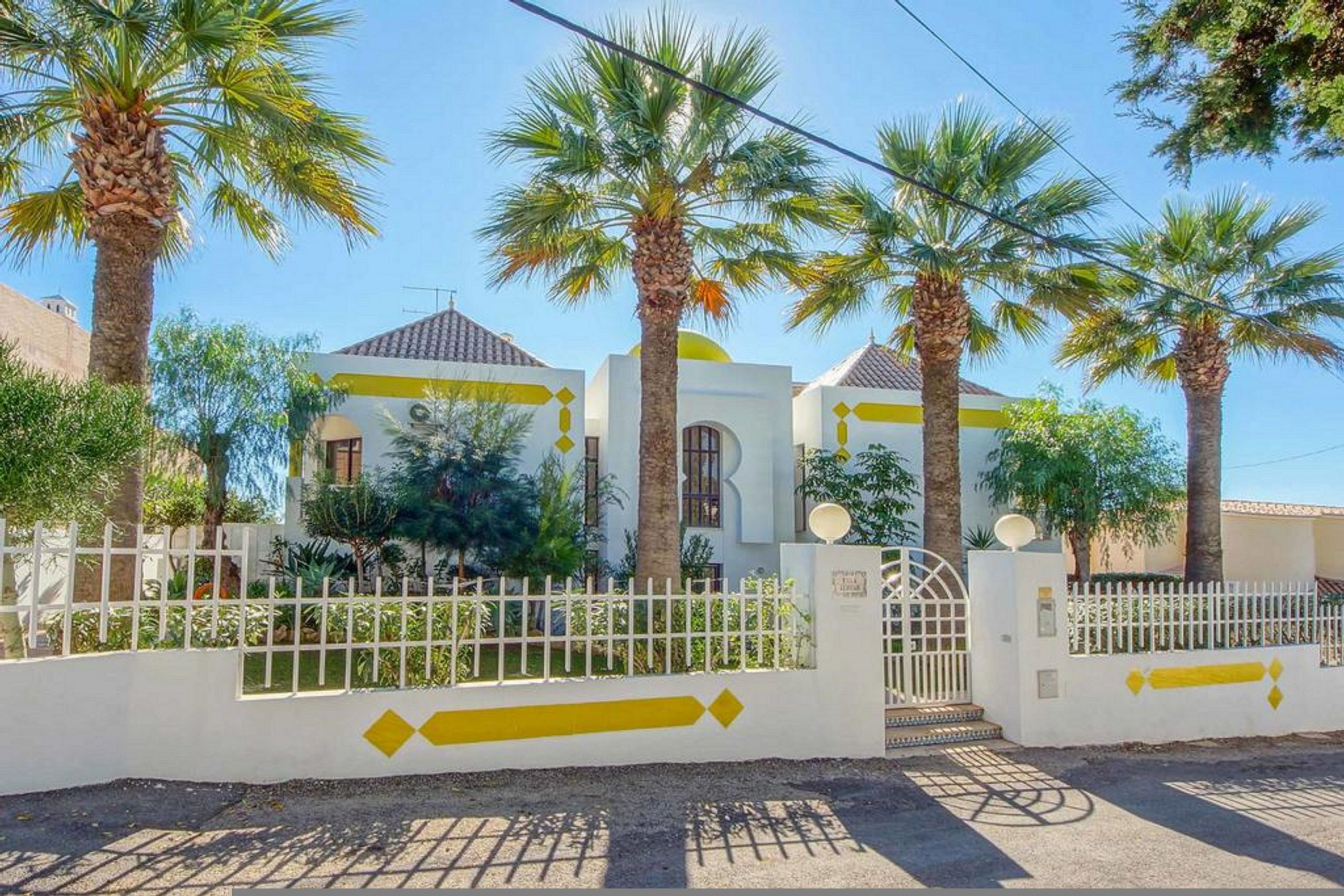 Un edifici residencial amb façana blanca, accents grocs i palmeres.