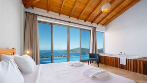 A bedroom with a large bed, a wooden ceiling, a view of the sea, and a bathroom with a bathtub. - Akasya Dio in Kalkan Belediyesi (Kalkan Belediyesi)