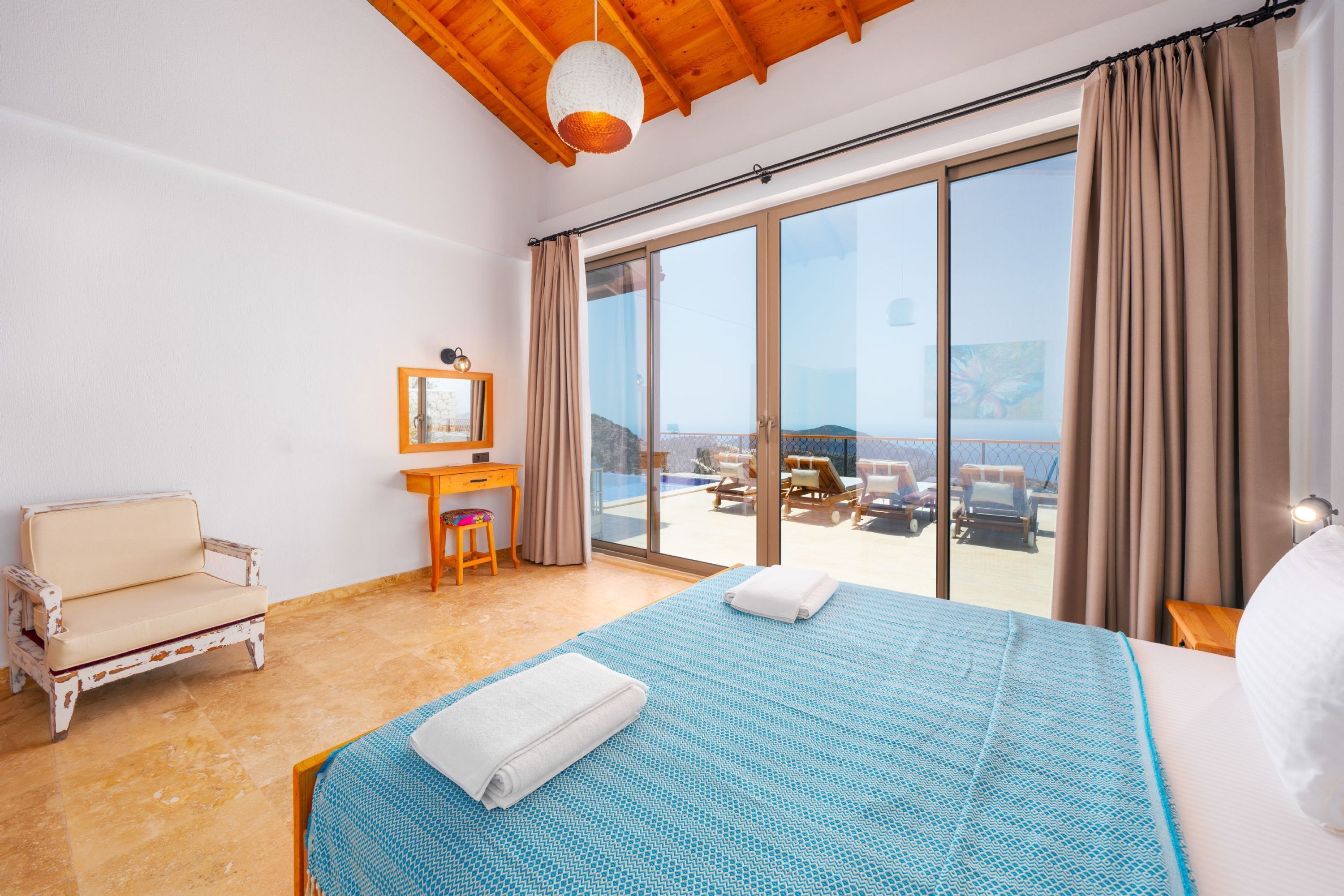 Ein Schlafzimmer mit einem großen Bett, einem Sessel, einem Schreibtisch und Blick auf den Balkon.