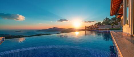Une piscine à débordement offrant une vue imprenable sur le coucher de soleil, la mer et les montagnes.