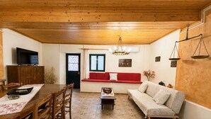 A wooden-floored living room with a dining area, a red sofa, and a chandelier. - Kansoneta-Traditional Mansion in Gastouri Village (Achilleio)