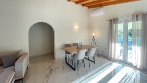Un salon moderne avec un plafond en bois, un coin repas comprenant une table et des chaises, un canapé et une grande fenêtre avec des rideaux.