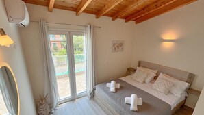 Une chambre avec un plafond en bois, un lit recouvert de draps blancs, une petite table et une fenêtre avec des rideaux.