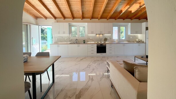 Une cuisine moderne avec des armoires blanches, un comptoir en marbre et un plafond en bois.