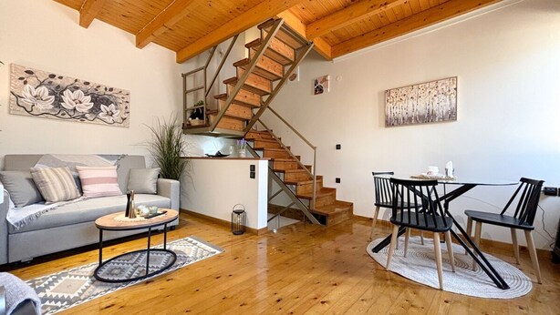 A spacious living area with a wooden staircase, a sofa, a coffee table, and a dining table with chairs. - Vilia Port House- Corfu Centre (Kerkira)