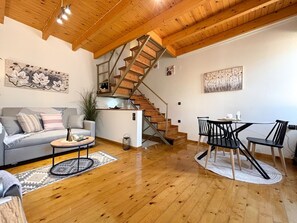 A spacious living area with a wooden staircase, a sofa, a coffee table, and a dining table with chairs. - Vilia Port House- Corfu Centre (Kerkira)