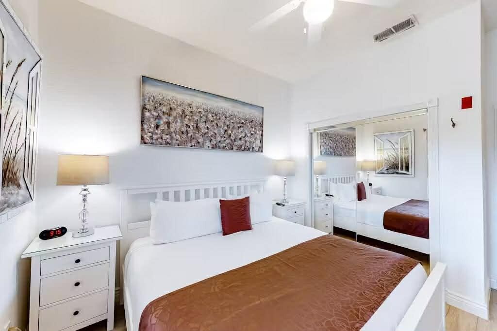 A hotel room with a large bed, a bedside table with a lamp, a mirror, and a painting on the wall.