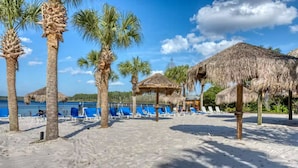 Una playa con palmeras, cabañas de techo de paja y sillas reclinables azules.
