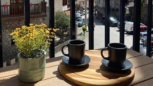 Ein Balkon mit einem Holztisch, zwei schwarzen Tassen und einem Topf mit einer gelben Blume.