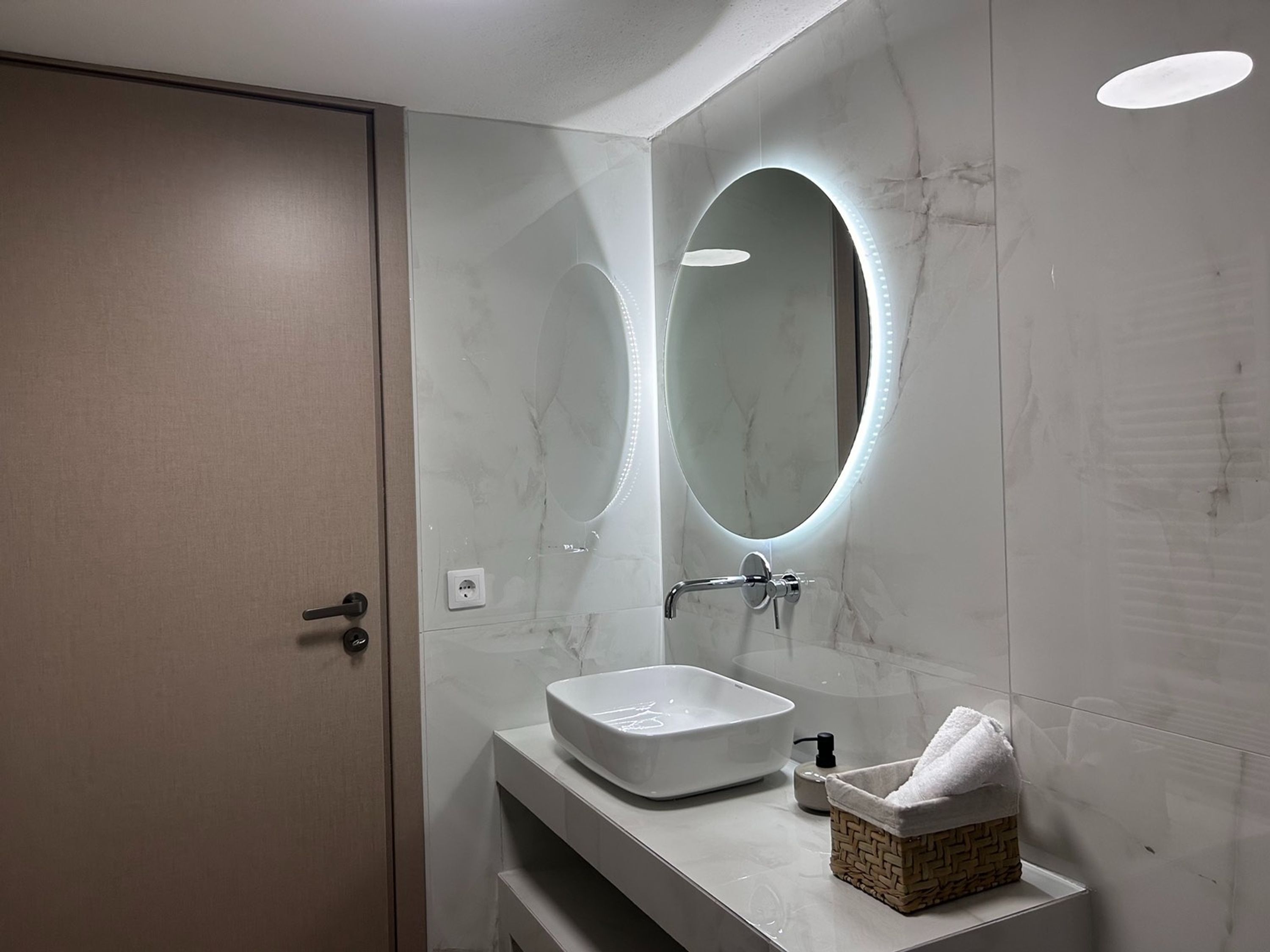 Un baño moderno con un espejo ovalado grande, un lavabo rectangular y un cesto para toallas.