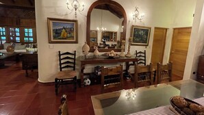 Un coin repas avec une table en bois, des chaises et une table avec un plateau en verre. Les murs sont ornés de tableaux et un lustre est suspendu au-dessus de la table.