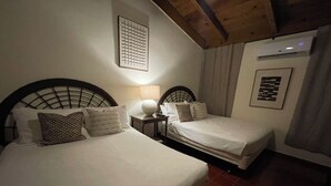 Une chambre d’hôtel avec deux lits, une table de chevet, une lampe, un appareil de climatisation et un tableau encadré au mur.